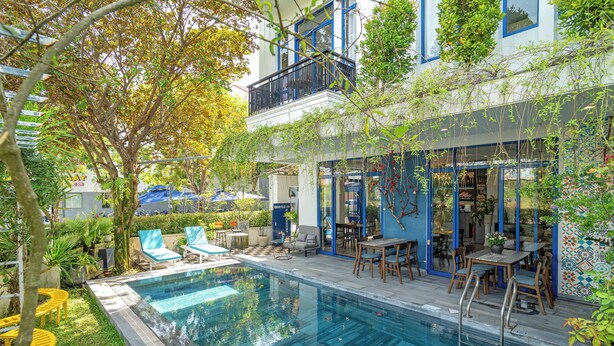 A pool area with lounge chairs, a table, and a covered patio with chairs and a table. - Blue Boutique Villa Hoi An (Da Nang)
