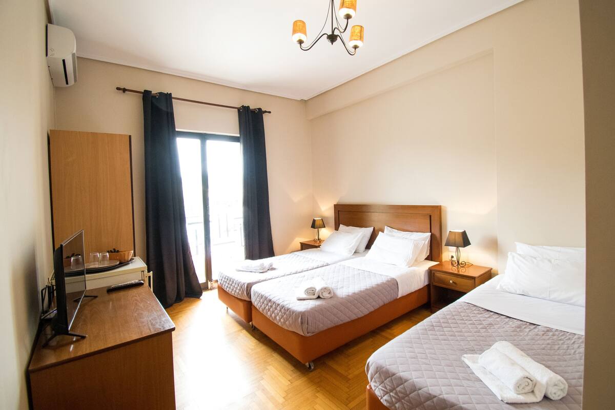 A hotel room with two beds, a desk with a computer, a TV, and a window with curtains.