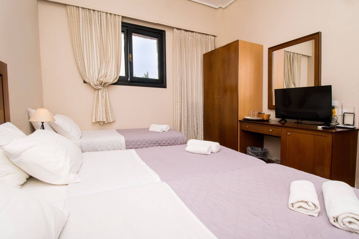 A hotel room with two beds, a TV, a desk, and a window with curtains.