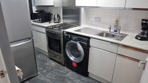A compact kitchen with a stainless steel refrigerator, a built-in oven, a washing machine, a coffee maker, and a sink. - North London Apartment - Edmonton (London)