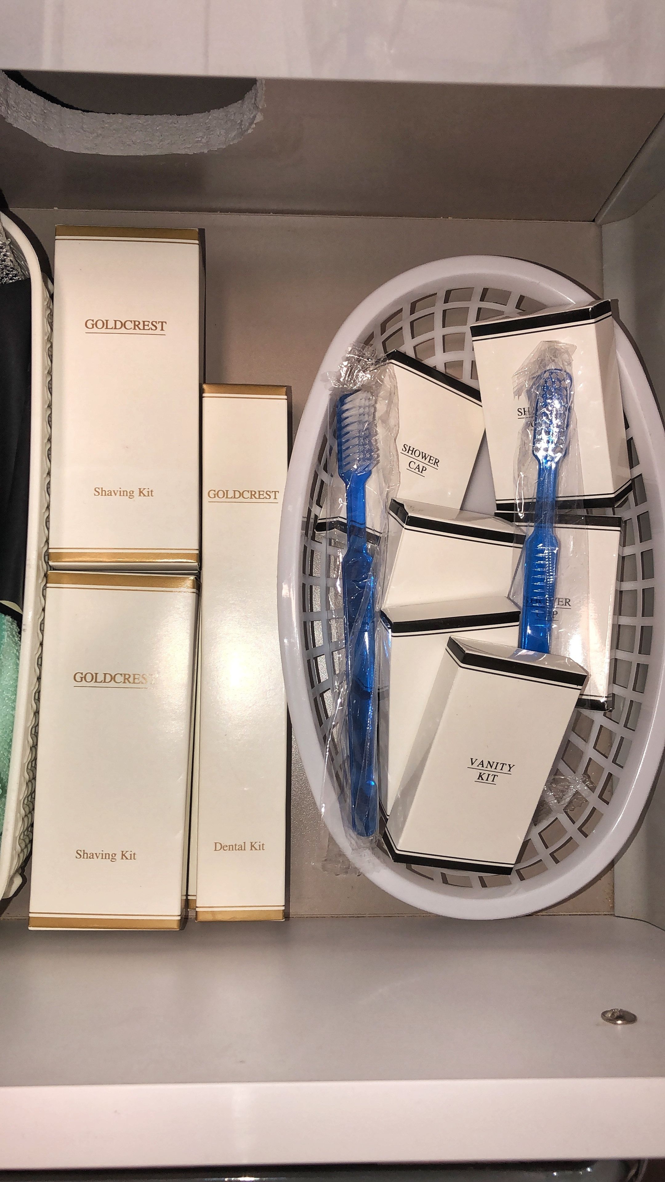 A bathroom with a white sink, a mirror, and a shelf with various toiletries including shaving kits, dental kits, and a shower cap.