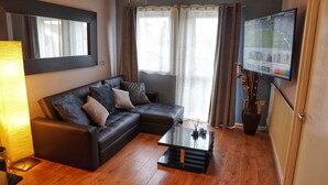 A modern living room with a sectional sofa, a glass coffee table, and a flat-screen TV mounted on the wall. - North London Apartment - Edmonton (London)