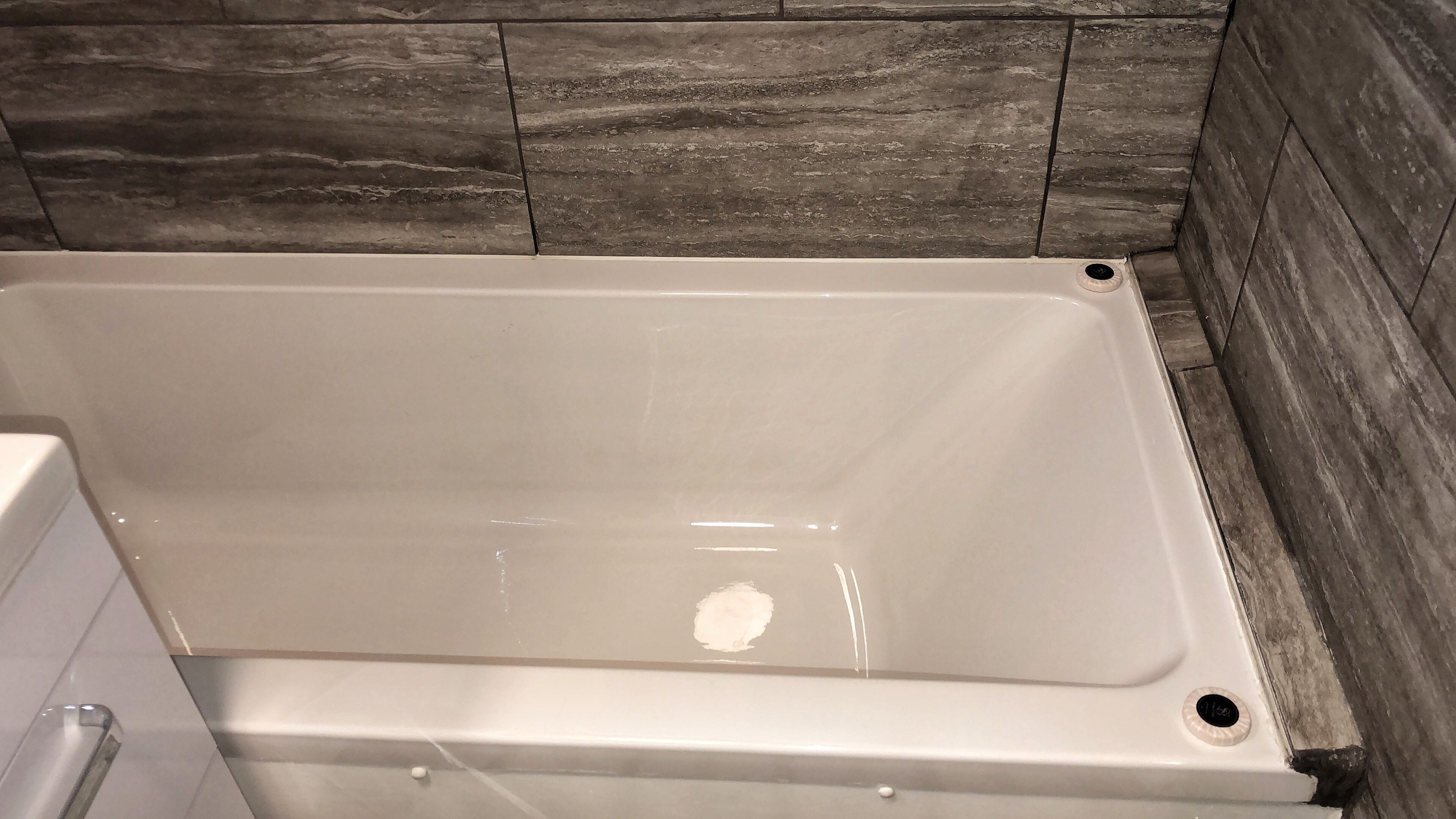 Una bañera blanca de forma rectangular, ubicada frente a una pared con un diseño de baldosas oscuras y texturizadas.