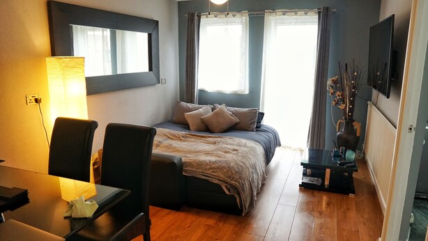 A compact bedroom with a bed, bedside table, chair, and a desk with a lamp. - North London Apartment - Edmonton (London)