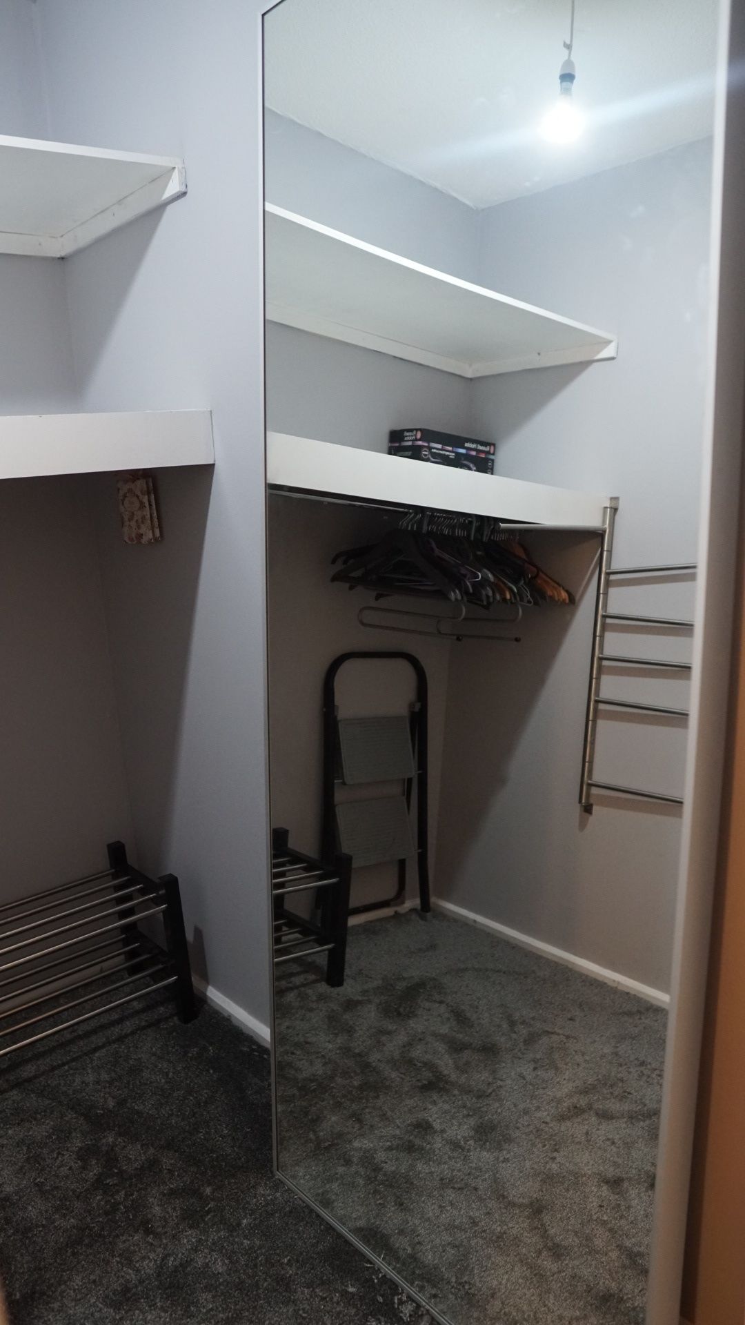 A compact walk-in closet with a mirrored closet door, a metal drying rack, and a small chair.