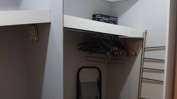 A compact walk-in closet with a mirrored closet door, a metal drying rack, and a small chair.