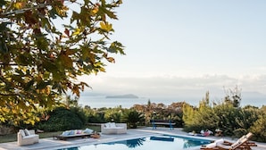 Uma área de piscina com espreguiçadeiras, um banco e vista para o mar.