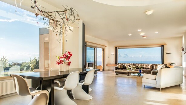 Uma sala de estar moderna com área de jantar, janelas amplas e vista para o mar.