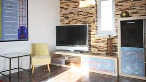 A living room with a flat-screen TV on a wooden entertainment unit, a striped armchair, and a large abstract painting on the wall. - Schöne 3Zimmer FeWo direkt am Baalensee (Fürstenberg-Havel)