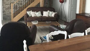 A living room with a brown sofa, two armchairs, a wooden coffee table, and a staircase with wooden railings.