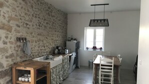 A compact kitchen with a stone wall, wooden counter, and a window with potted plants.