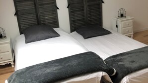 A bedroom with a sloped ceiling, two beds with dark headboards, white bedding, a white nightstand with a lamp, and a wooden floor.