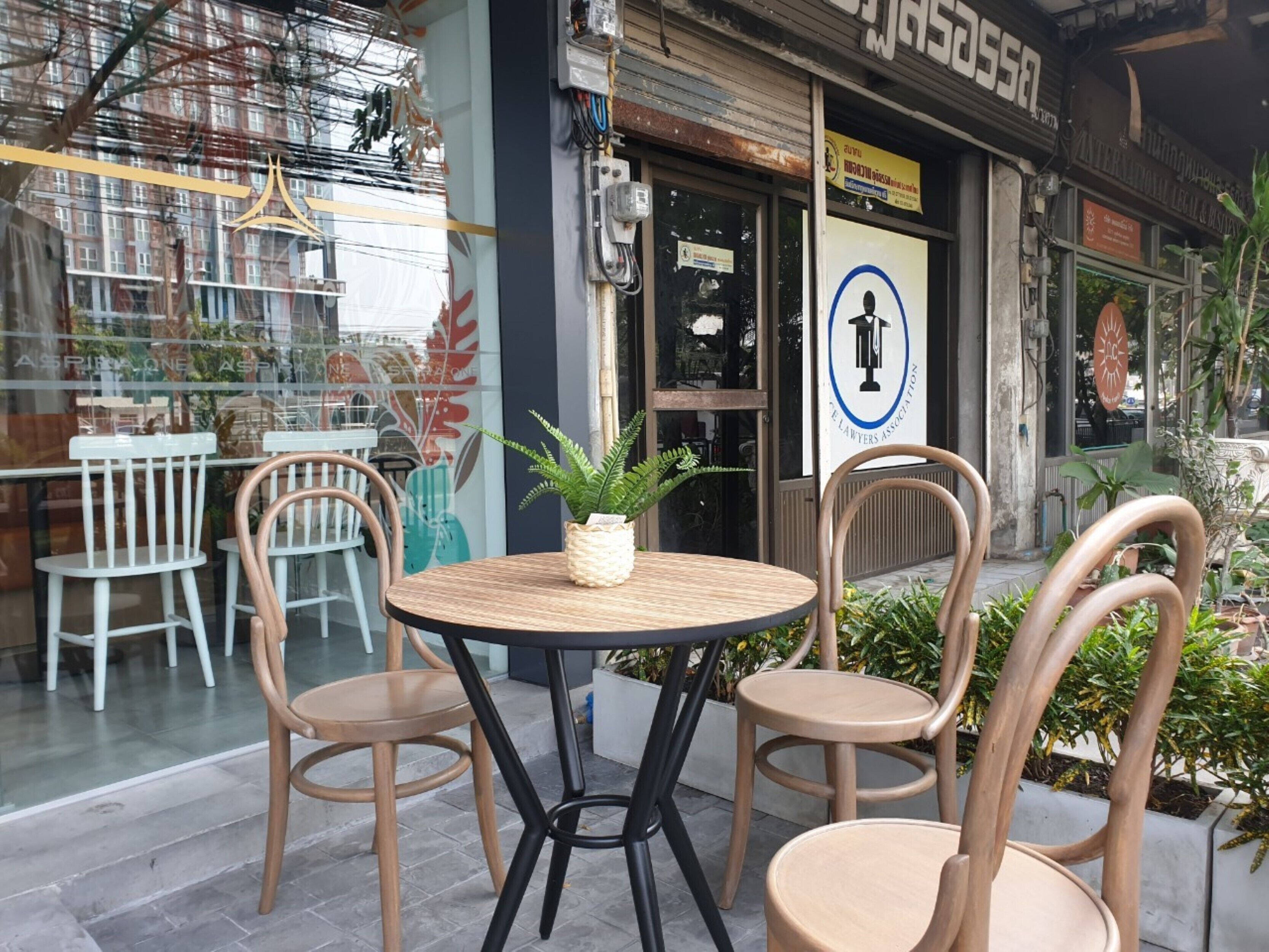 Un espace extérieur aménagé avec des tables et des chaises rondes, un pot de fleurs et un mur de verre donnant sur un bâtiment avec une enseigne.