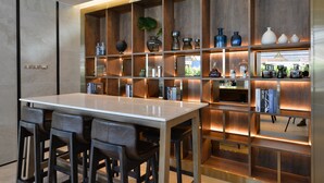 A modern kitchen with a central island, wooden shelving with decorative items, and bar stools. - Aspira One Sutthisan (Bangkok)