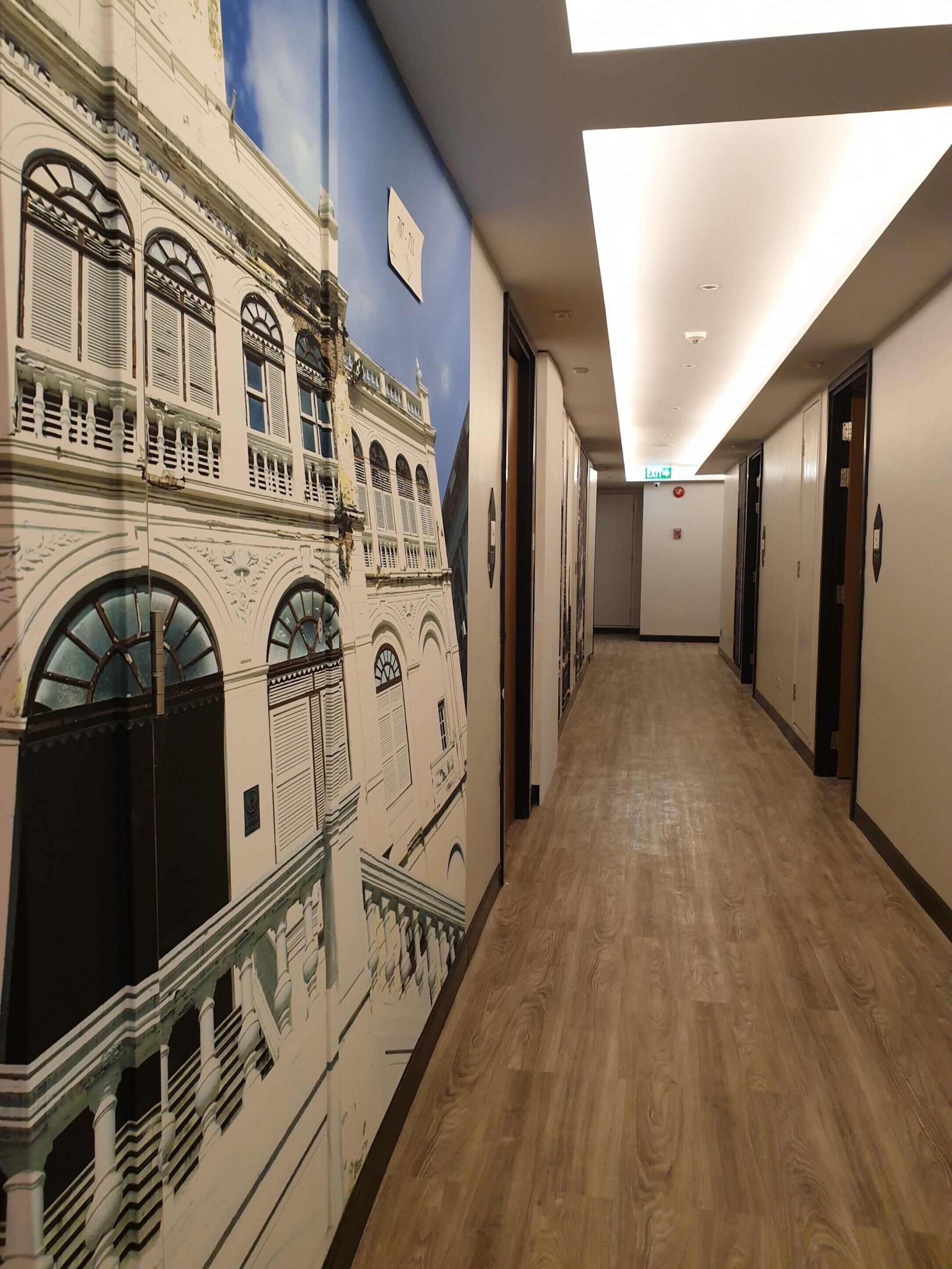 Pasillo de hotel con un mural de un edificio histórico, suelo de madera y puertas que dan a las habitaciones.