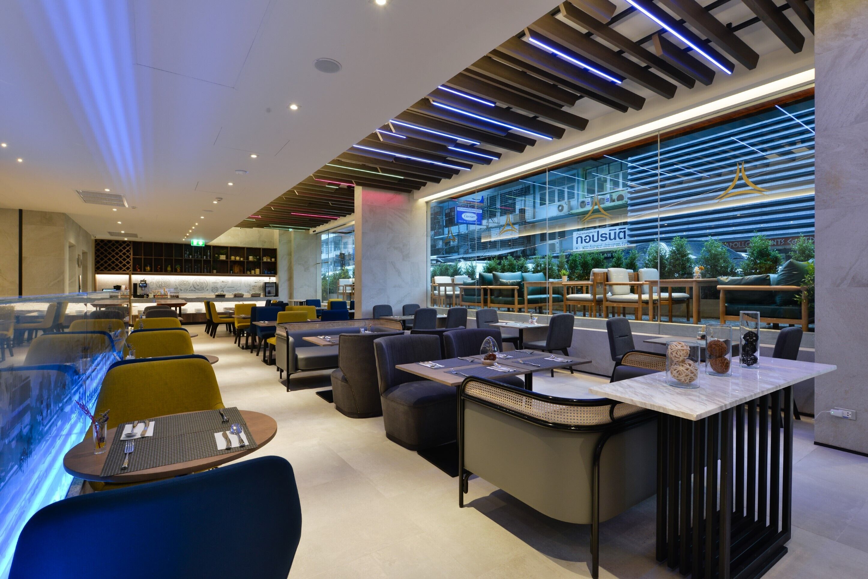 A modern restaurant with a variety of seating options including booths and tables, a bar area with a glass partition, and a view of the cityscape through large windows.
