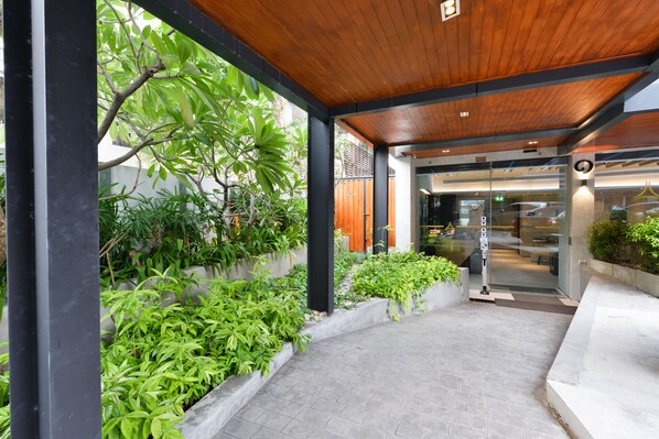 A covered entrance with a wooden ceiling, a glass door, and a pathway leading to a building.