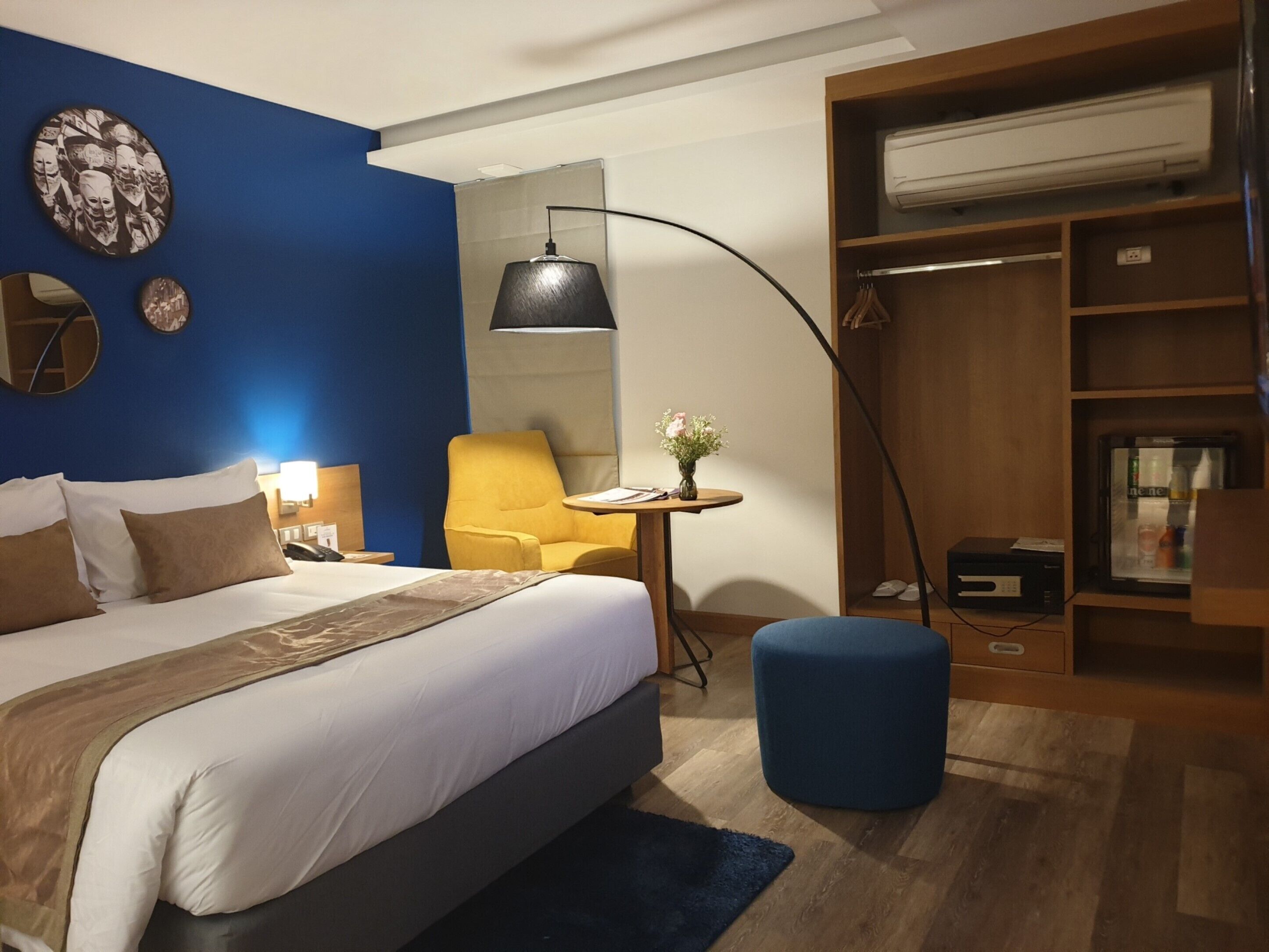 Hotellihuone, jossa on sänky, työpöytä, tuoli, vaatekaappi ja pieni pöytä, jonka päällä on maljakko täynnä kukkia.