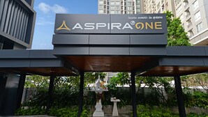 A sign for "ASPIRA ONE" with a modern architectural design, surrounded by greenery and urban buildings. - Aspira One Sutthisan (Bangkok)