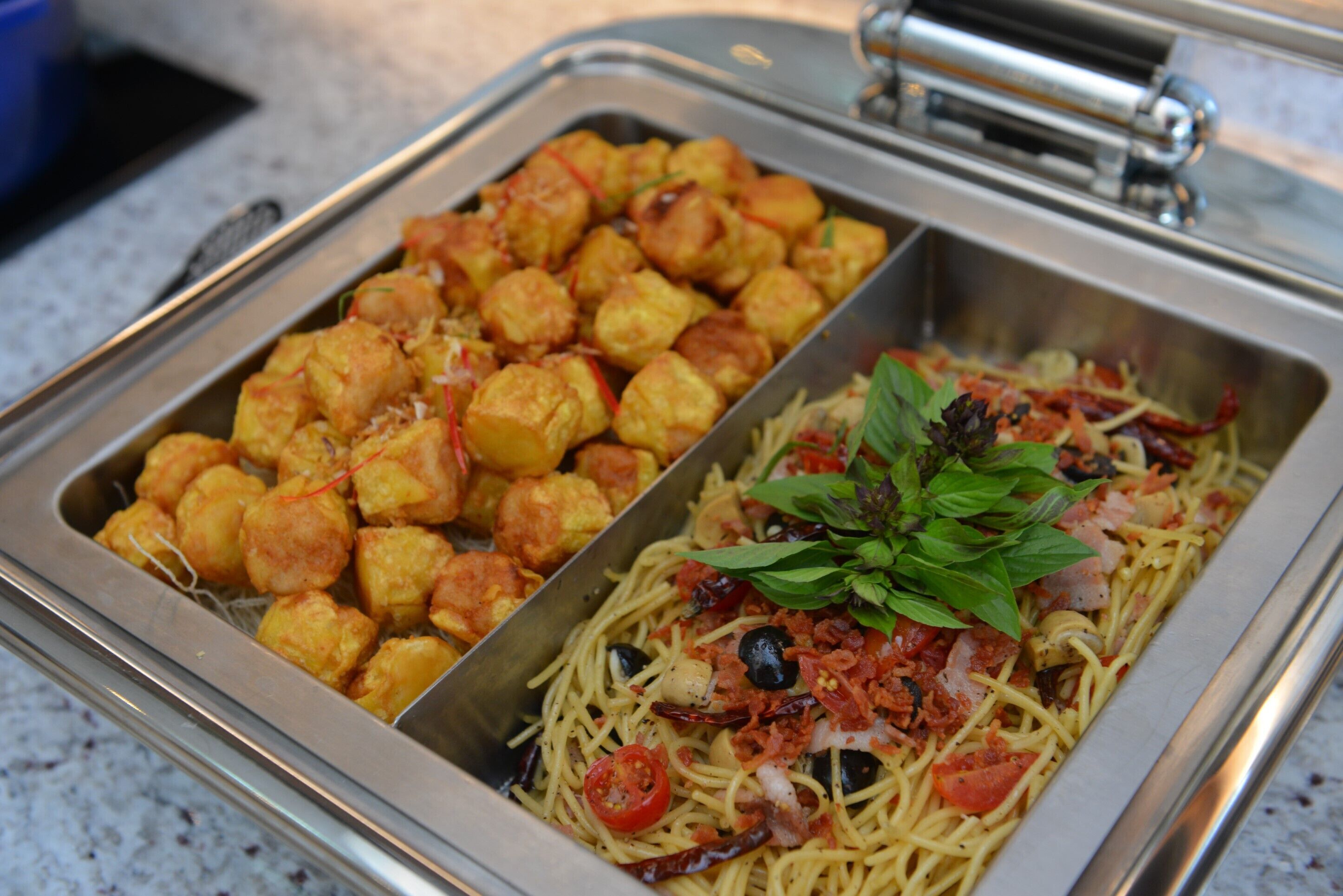 Un buffet diviso in due aree: una con cibi fritti e l'altra con pasta guarnita con pomodori e basilico.