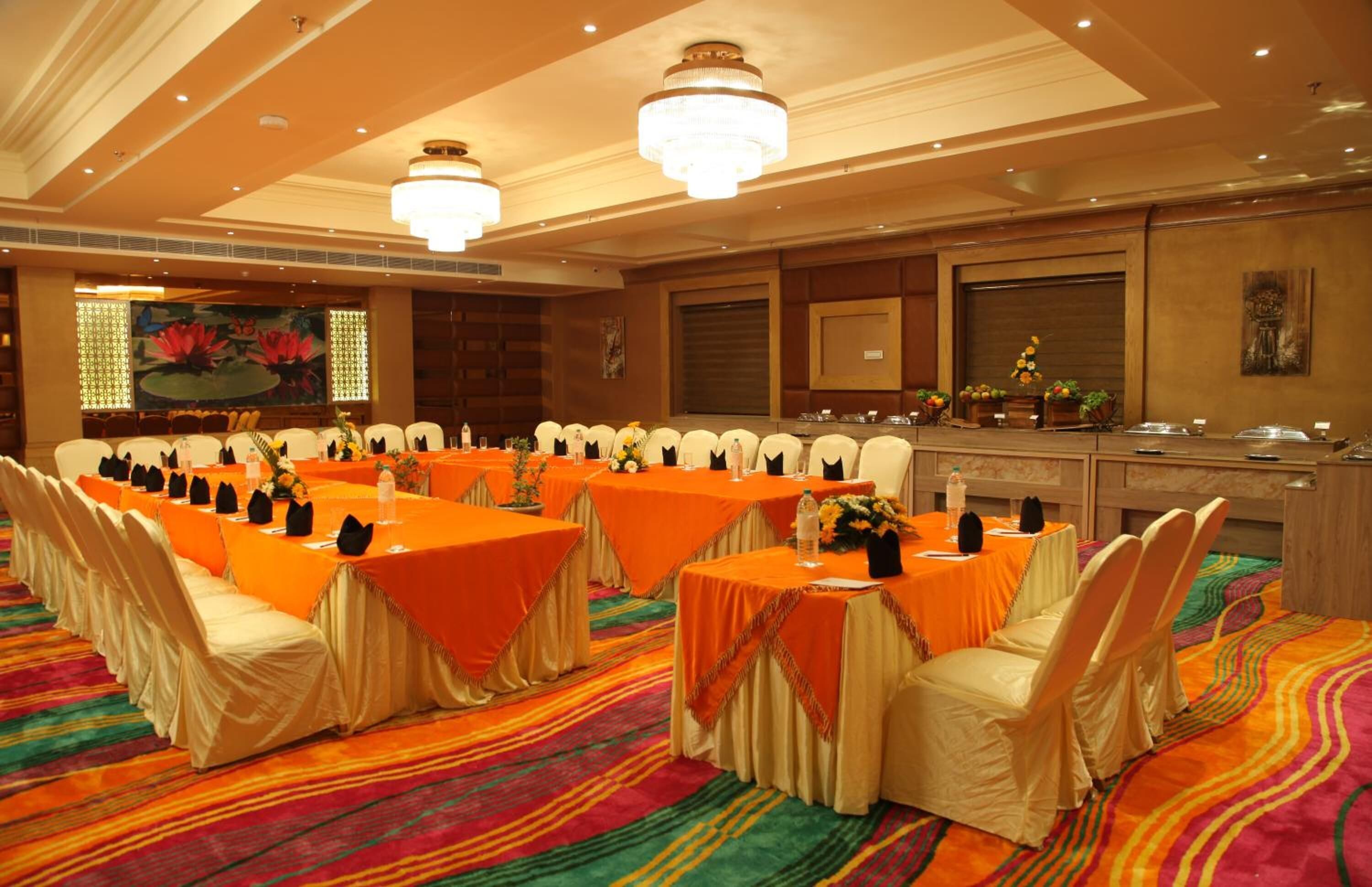 A banquet hall with multiple tables set for a meeting, featuring a colorful carpet and elegant chandeliers.