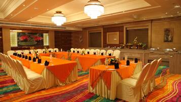 A banquet hall with multiple tables set for a meeting, featuring a colorful carpet and elegant chandeliers.