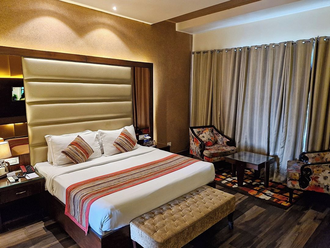 Habitación de hotel con una cama grande, una mesita de noche, una silla, una pequeña mesa y una ventana con cortinas.
