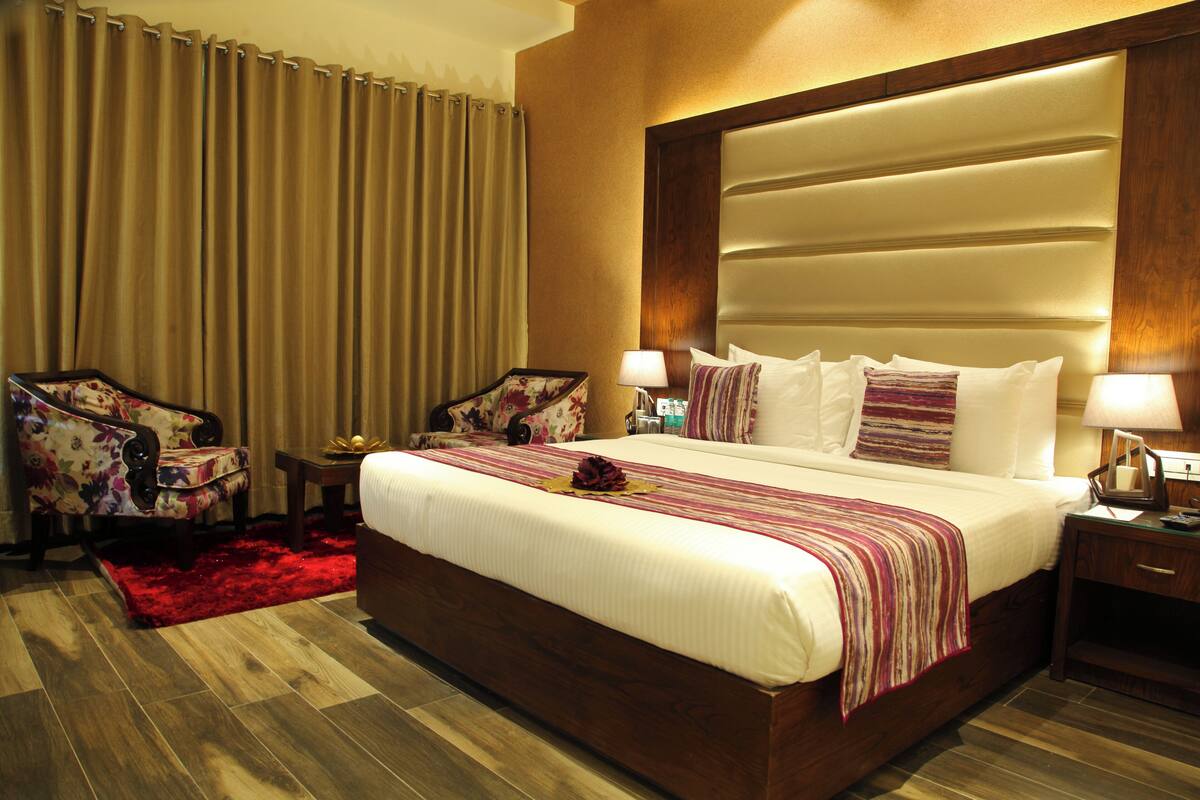 A hotel room with a large bed, a wooden headboard, a red rug, and a floral armchair.