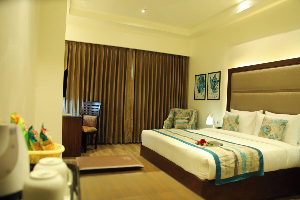 A hotel room with a large bed, a desk with a laptop, a chair, and a window with curtains.