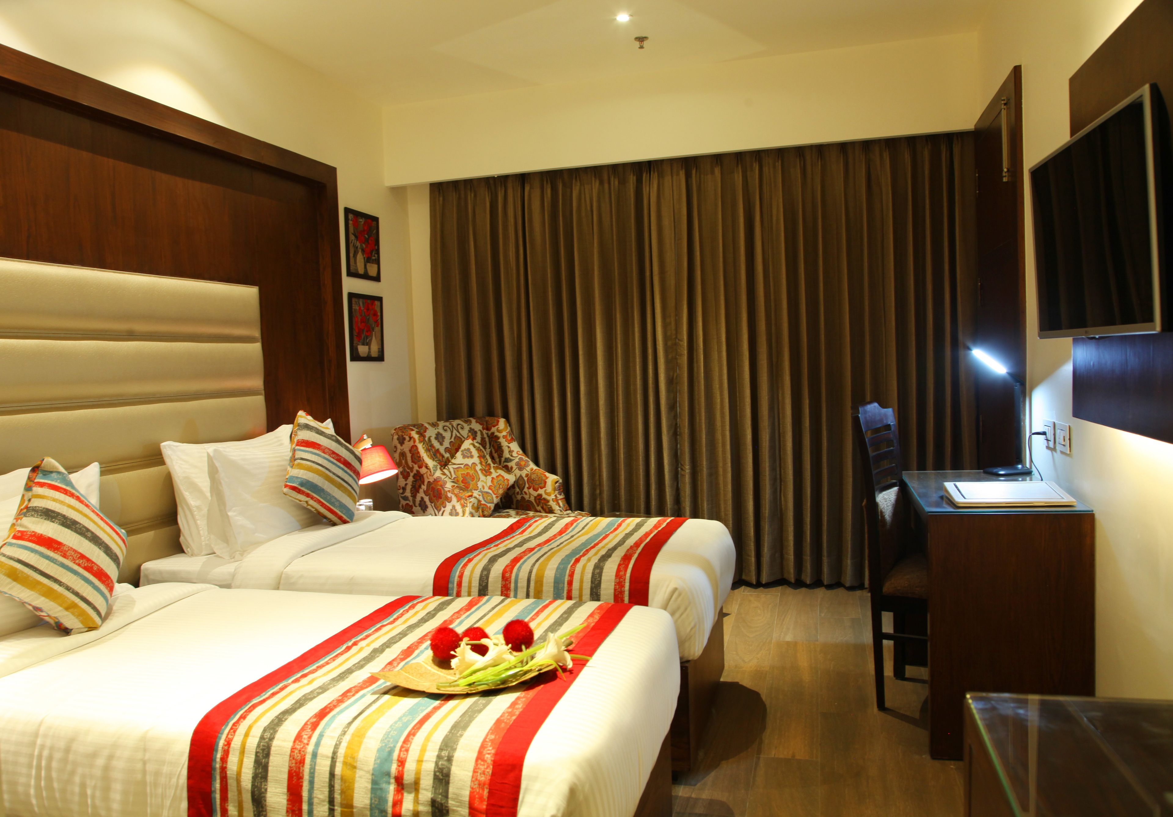 A hotel room with two beds, a desk, a chair, a television, and a large window with curtains.