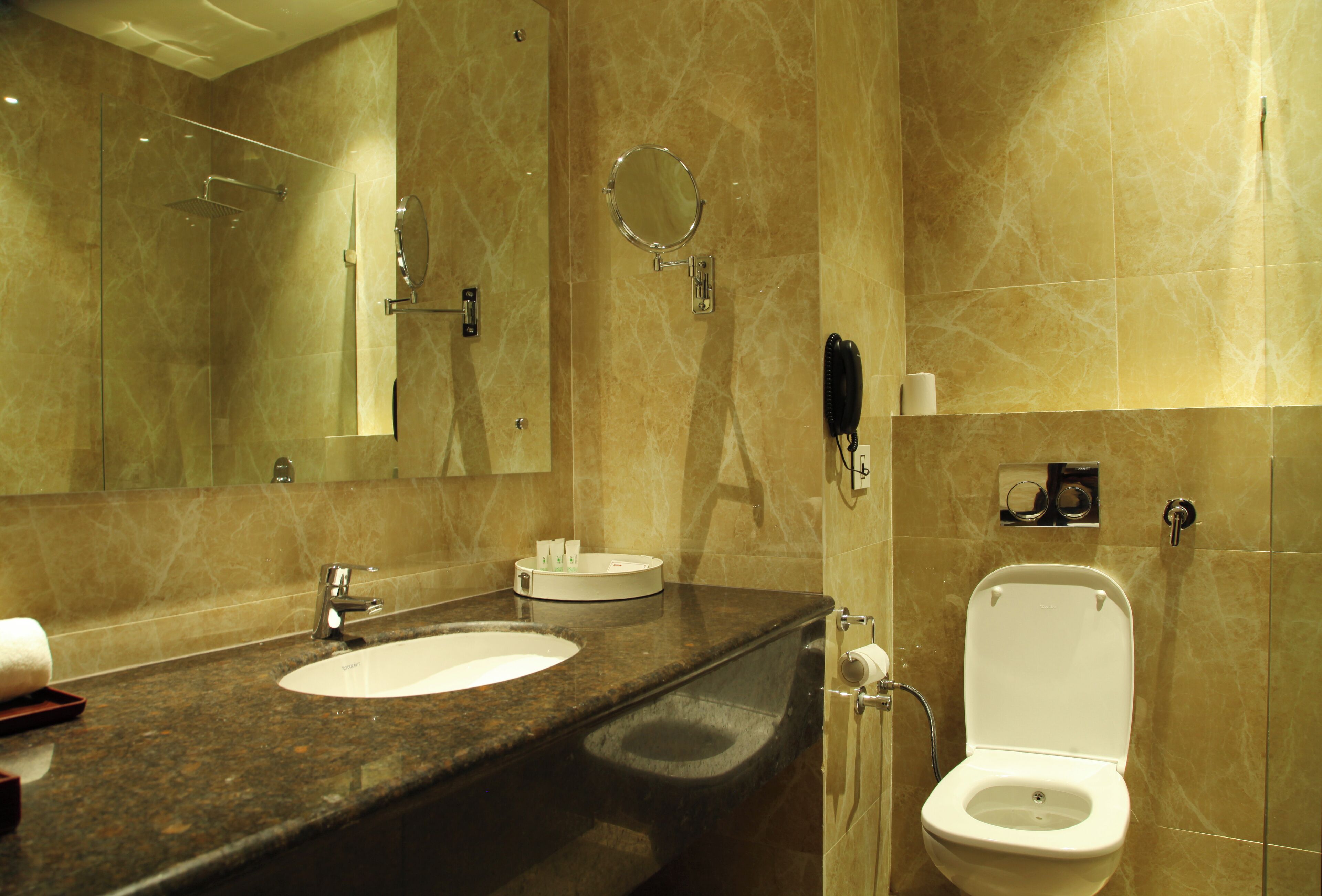 Un baño con lavamanos de mármol, un espejo, un inodoro y ducha con cerramiento de vidrio.
