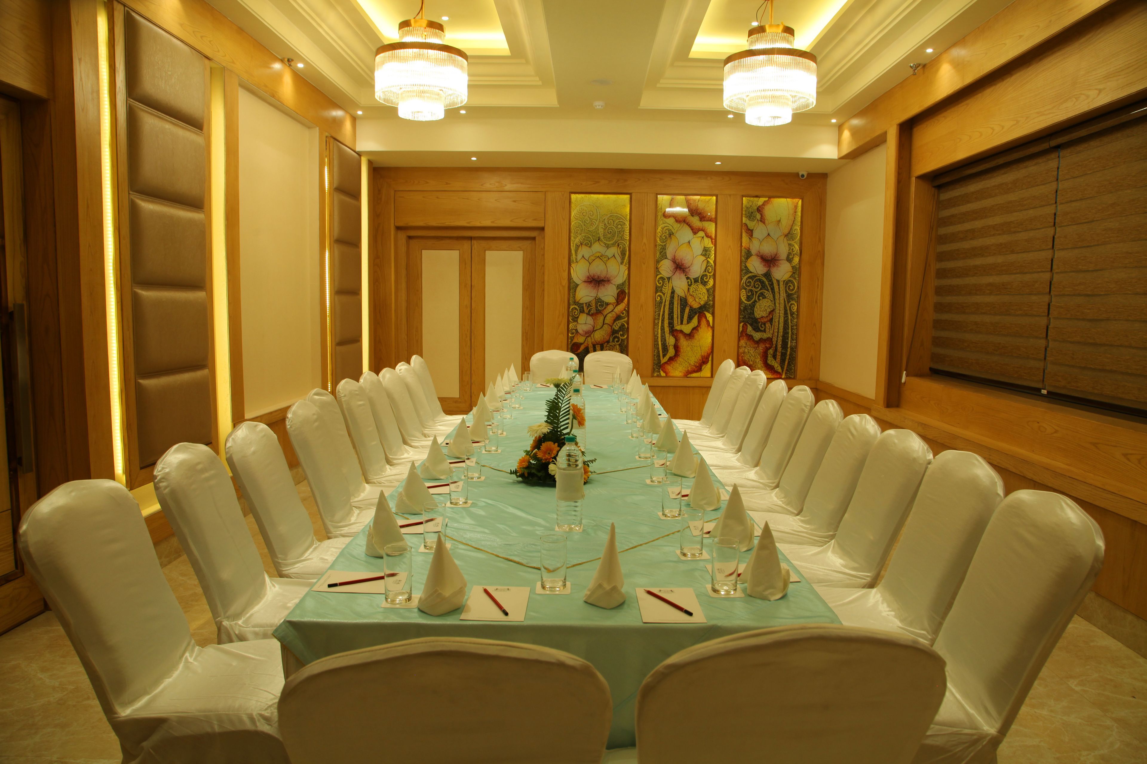 A conference room with a long table, white chairs, and chandeliers.