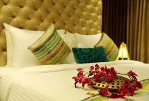 Una cama lujosa con almohadas a rayas y lisas, un objeto decorativo con forma de corazón y flores rojas sobre una colcha.