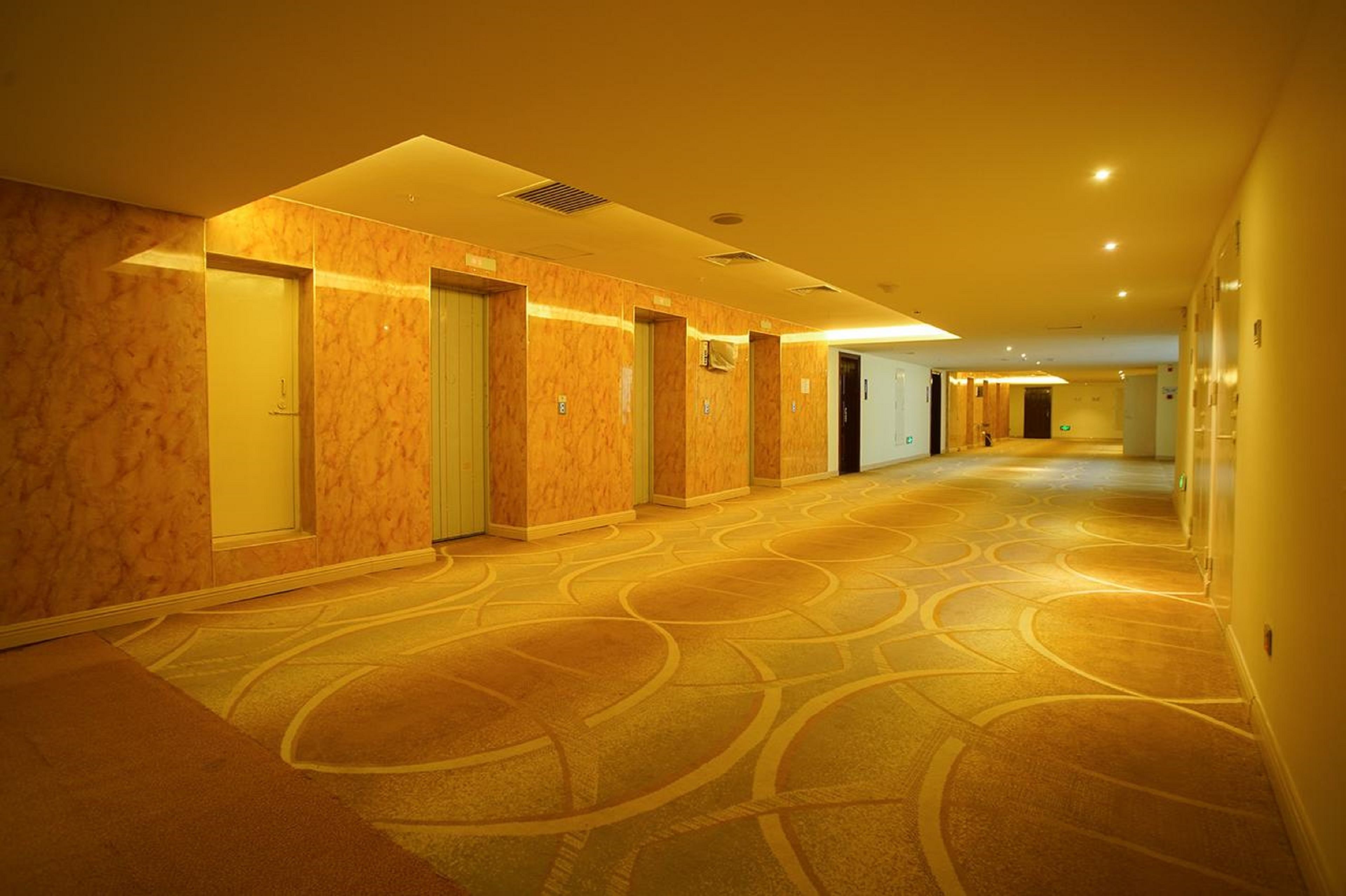 Un pasillo de hotel con paredes de mármol, puertas numeradas y alfombra estampada.