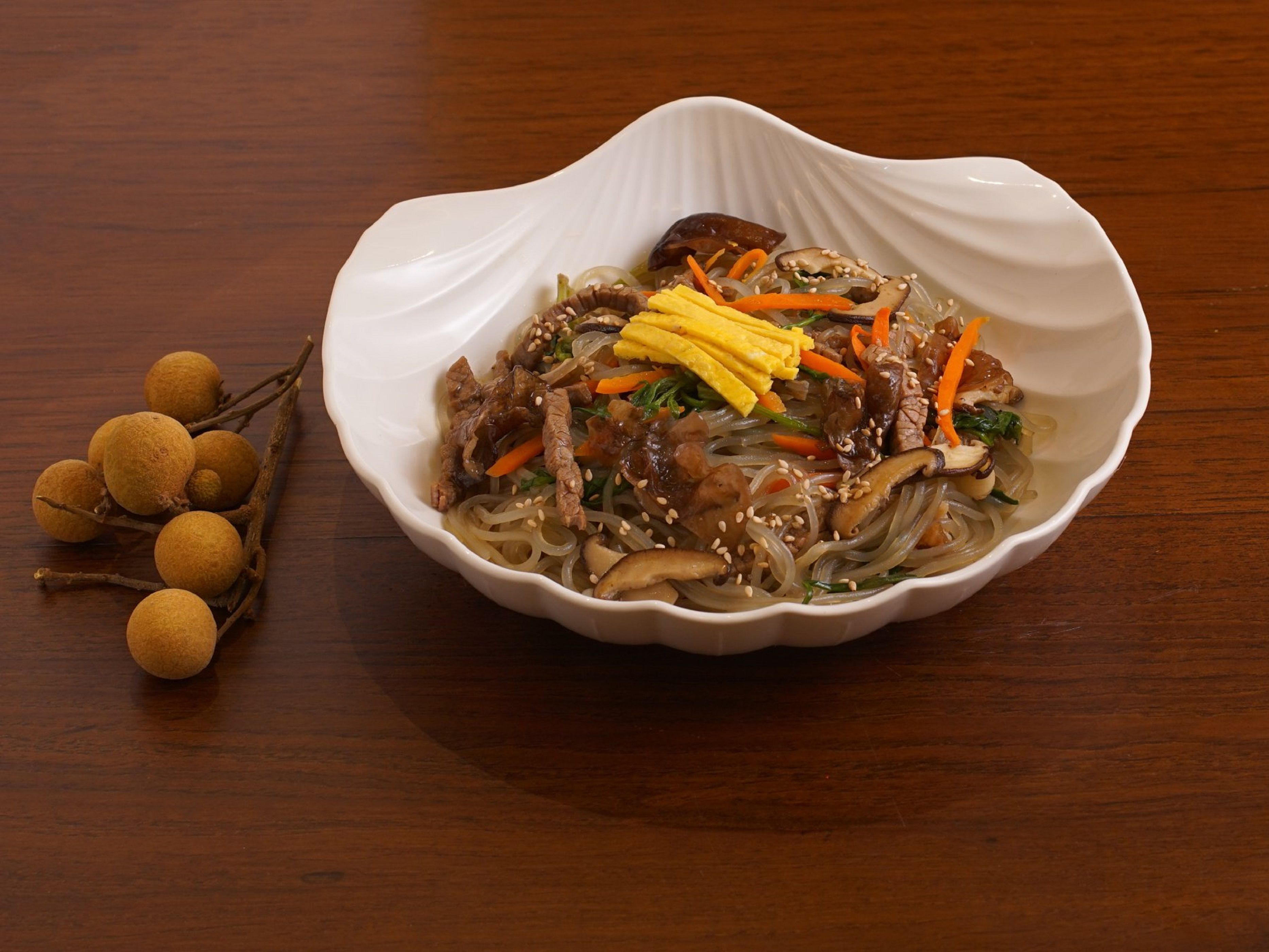 Un plat de cuisine asiatique composé de nouilles, de légumes et de viande, accompagné d’une branche de litchi.