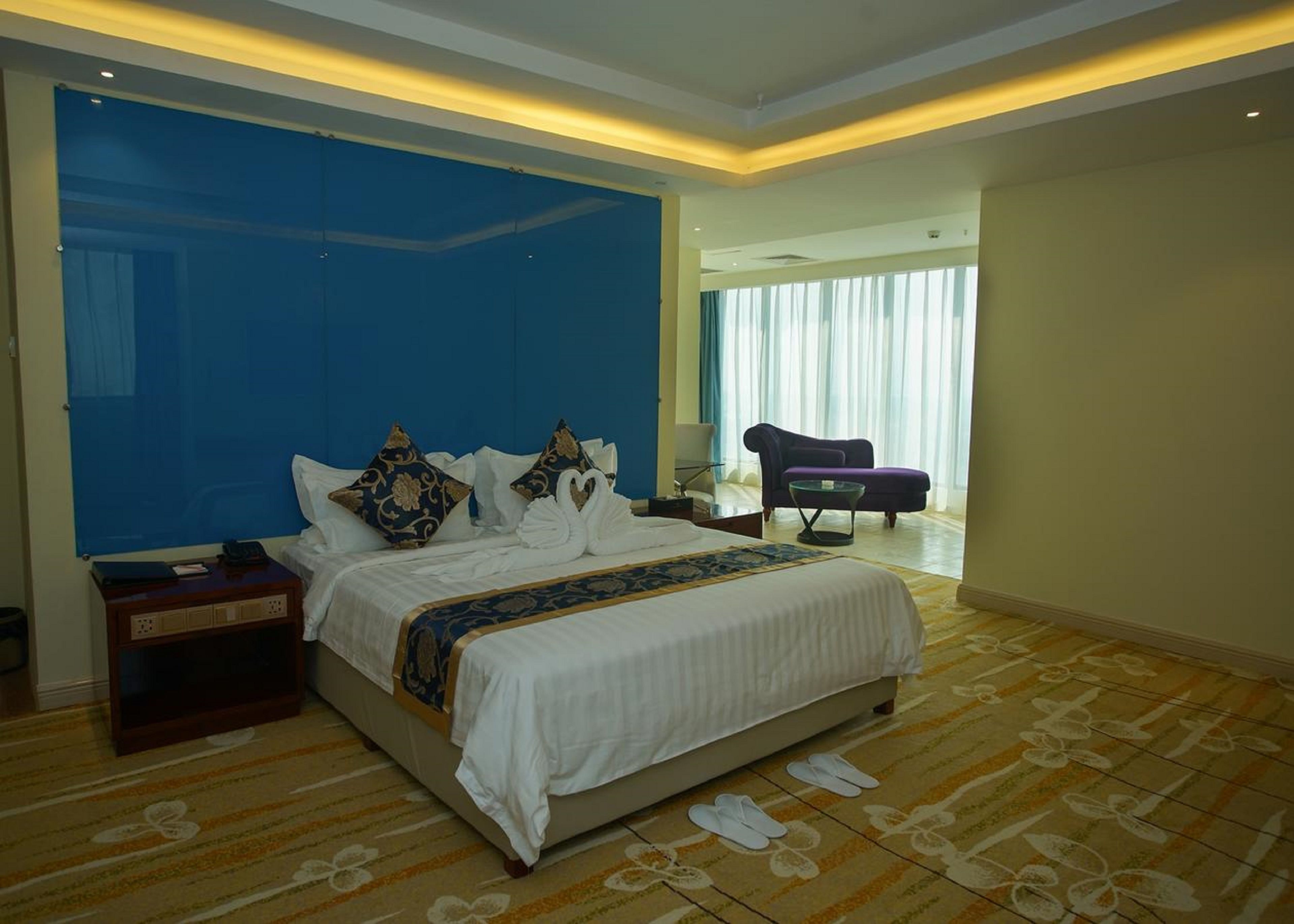 A hotel room with a large bed, a nightstand, a chair, and a view of the outside through a window.