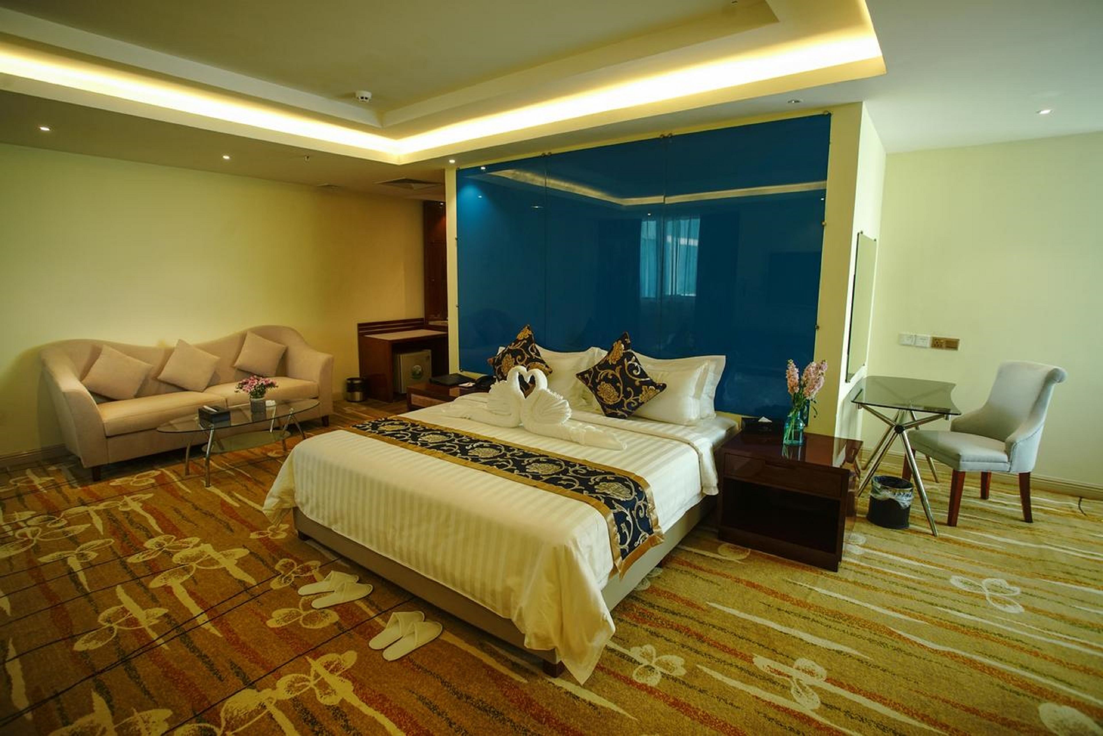 A hotel room with a large bed, a sofa, a small table, and a chair.