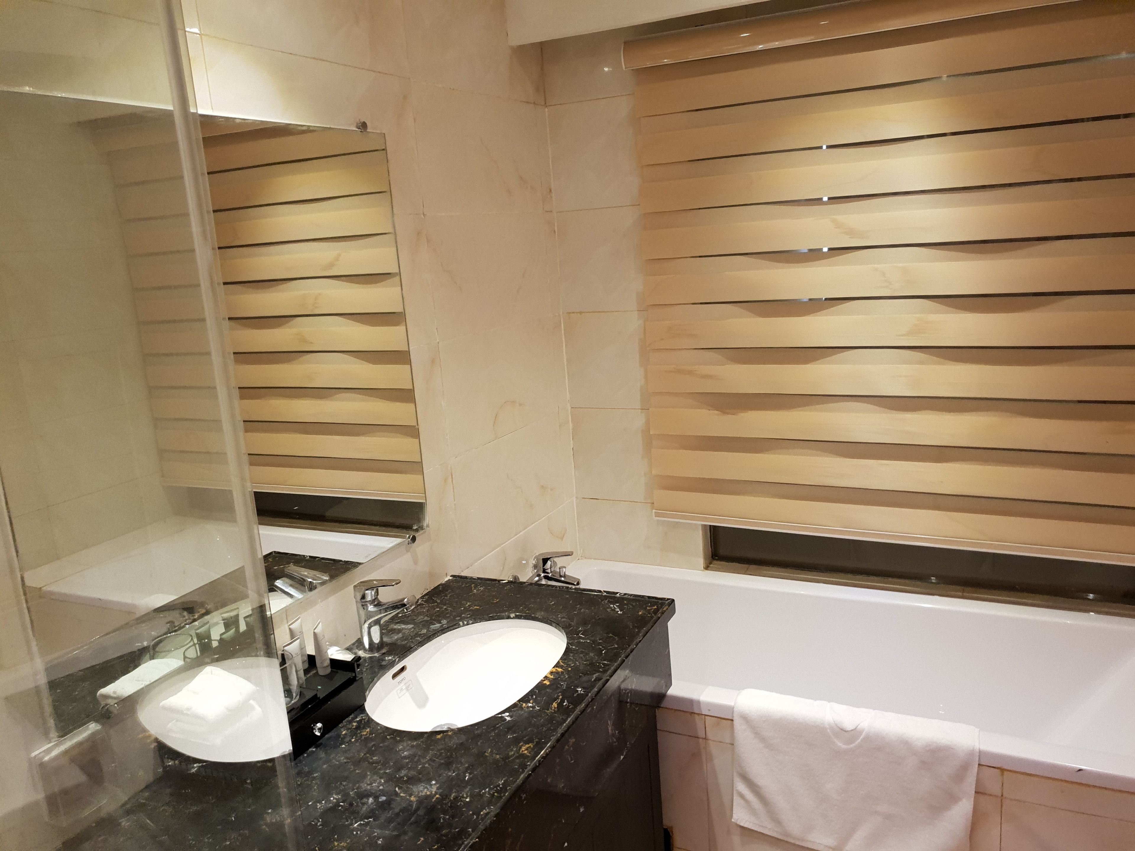 A bathroom with a black marble sink, a mirror, a white bathtub, and wooden slat blinds.