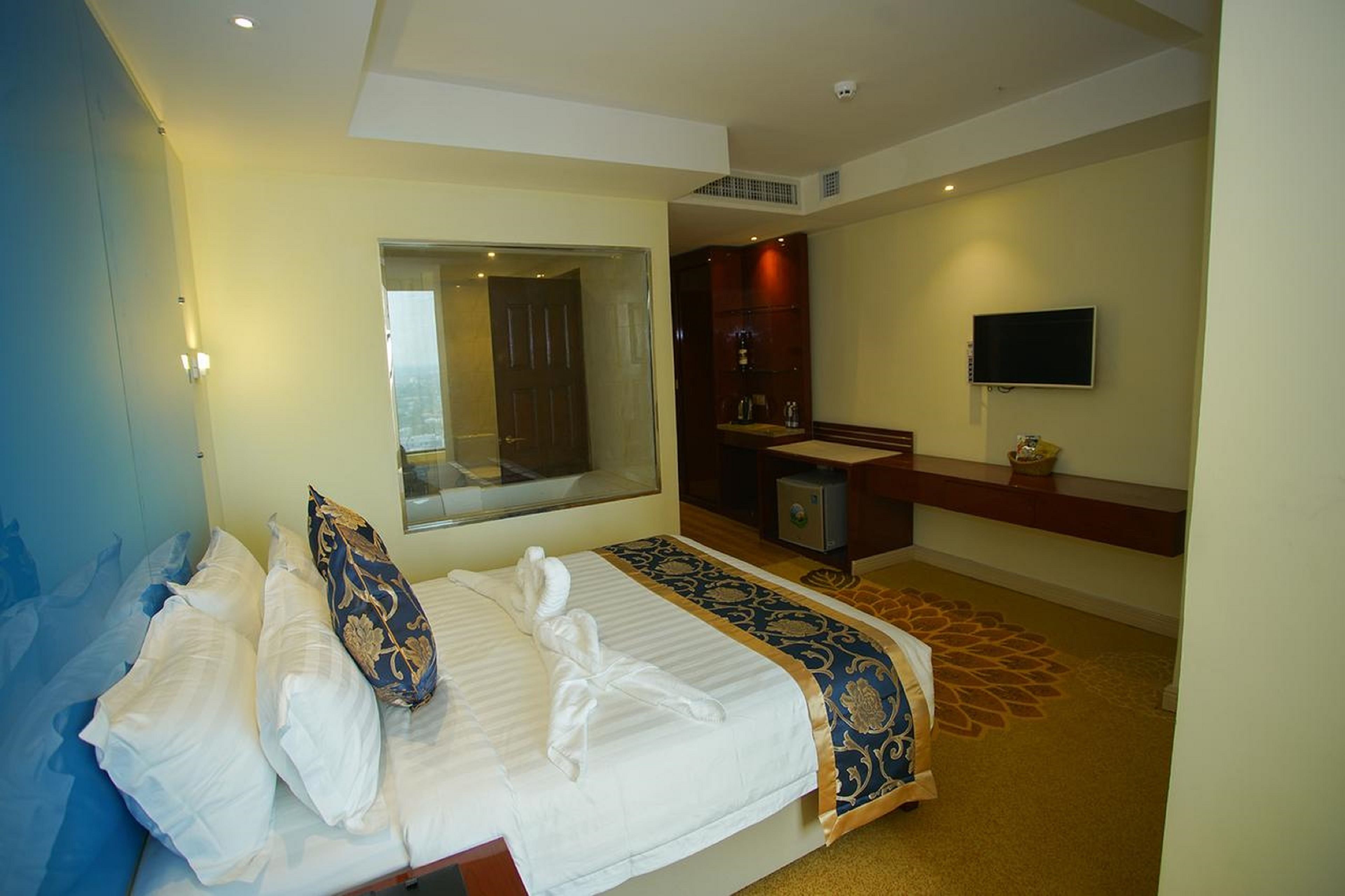 A hotel room with a large bed, a mirror, a television, and a bathroom with a sink and mirror.