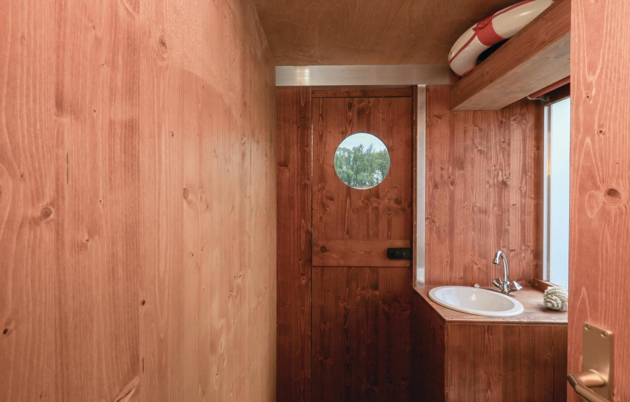 A wooden bathroom with a round mirror, a sink, and a window.