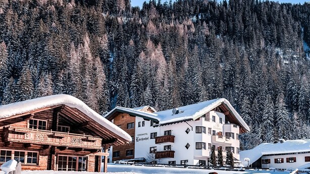 A snow-covered mountain lodge with wooden cabins and a white building labeled "Ferienhotel Larchhof."