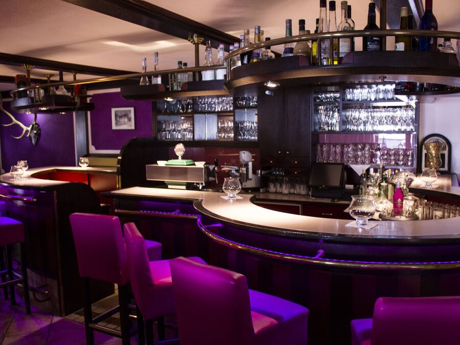 A bar area with purple lighting, bar stools, and shelves with bottles and glasses.