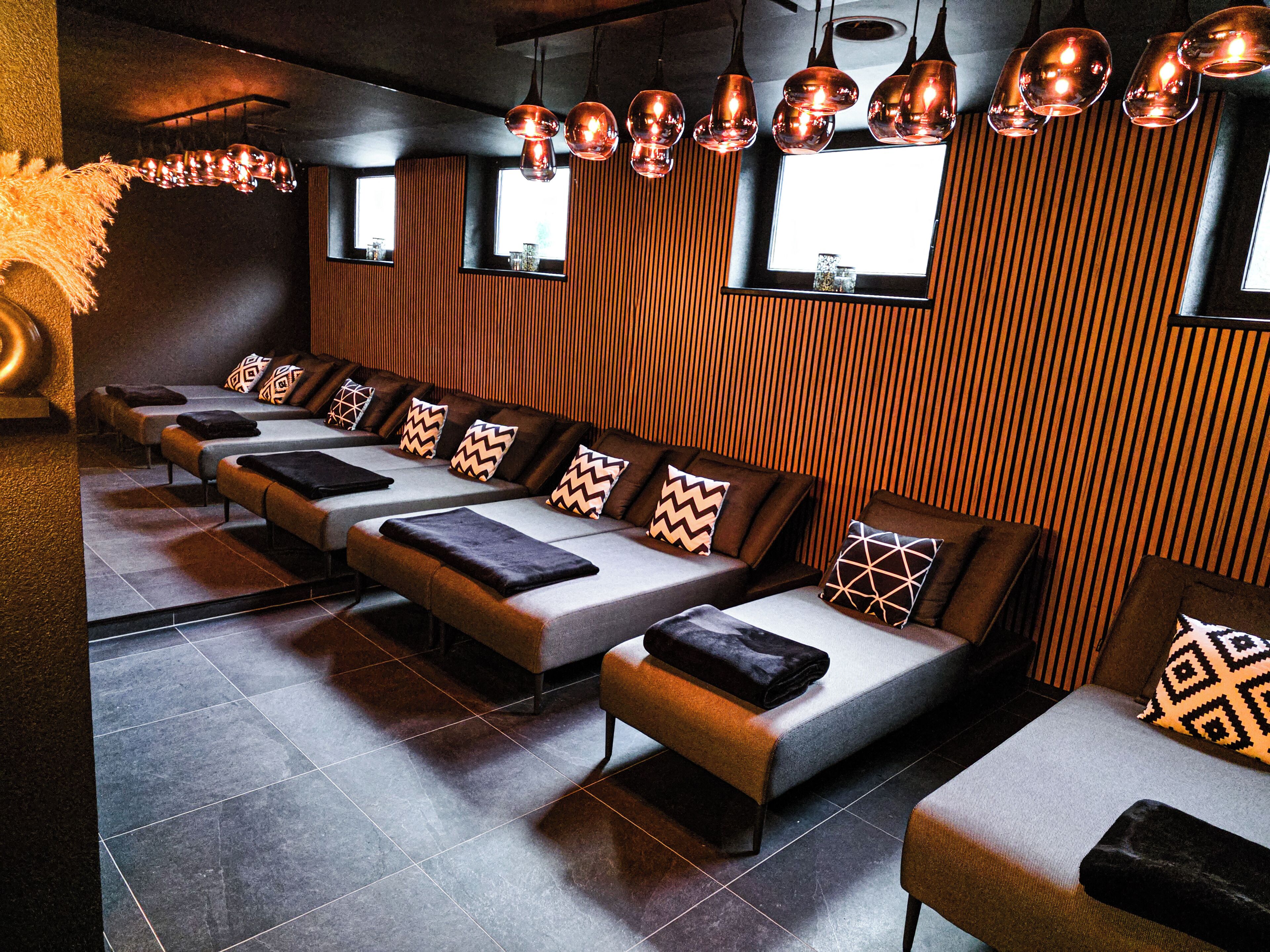 Una hilera de sillones de masaje con cojines estampados, un panel de madera con listones e iluminación colgante.