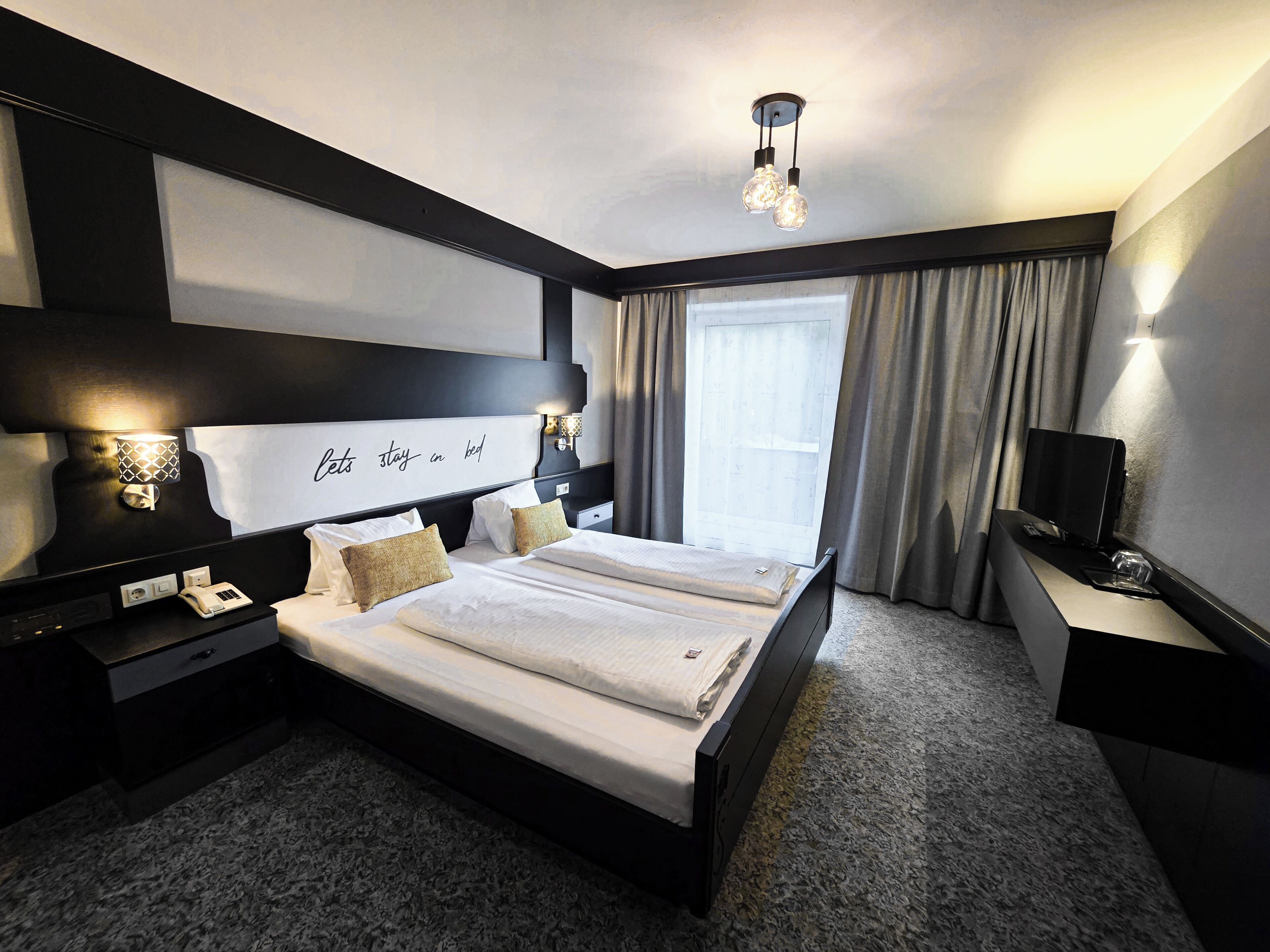 Una habitación de hotel con una cama grande, mesitas de noche, un escritorio, un televisor y una ventana con cortinas.