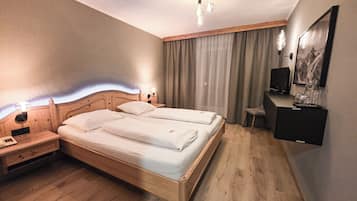 Hotellihuone, jossa on puinen sänky, työpöytä tuolilla, televisio ja taulu seinällä.