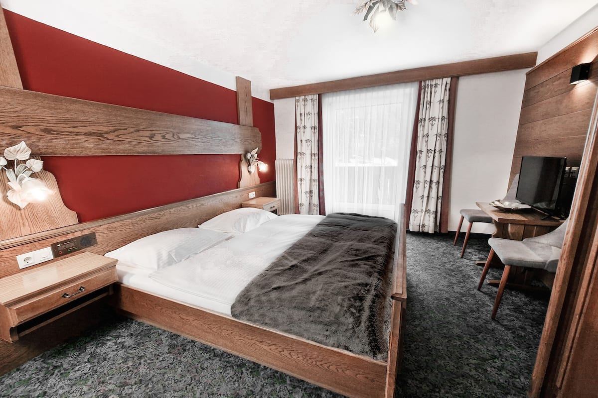 Una habitación de hotel con una cama de madera, un escritorio con una silla, un televisor y una ventana con cortinas.