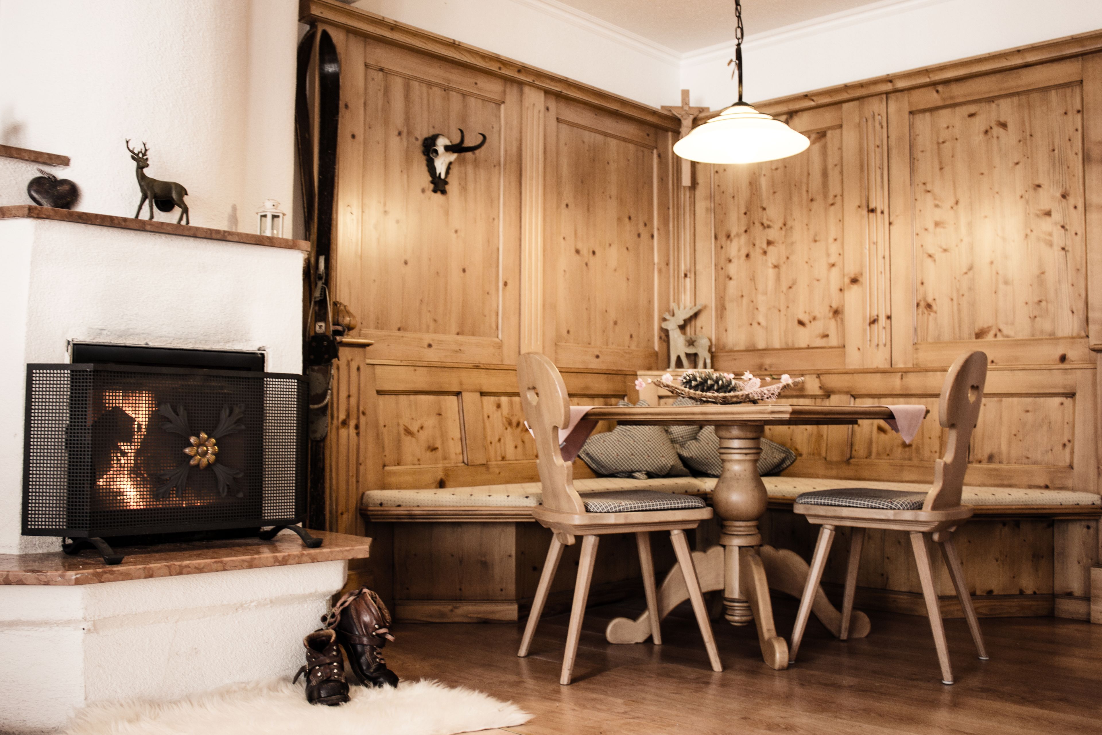Een kamer met houten lambrisering, een open haard, een tafel met stoelen en een hanglamp.