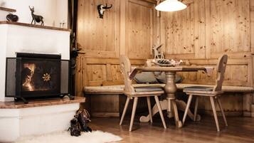 Een kamer met houten lambrisering, een open haard, een tafel met stoelen en een hanglamp.