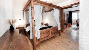 A four-poster canopy bed with a wooden frame and white drapes, a wooden nightstand, and a vase with dried pampas grass.