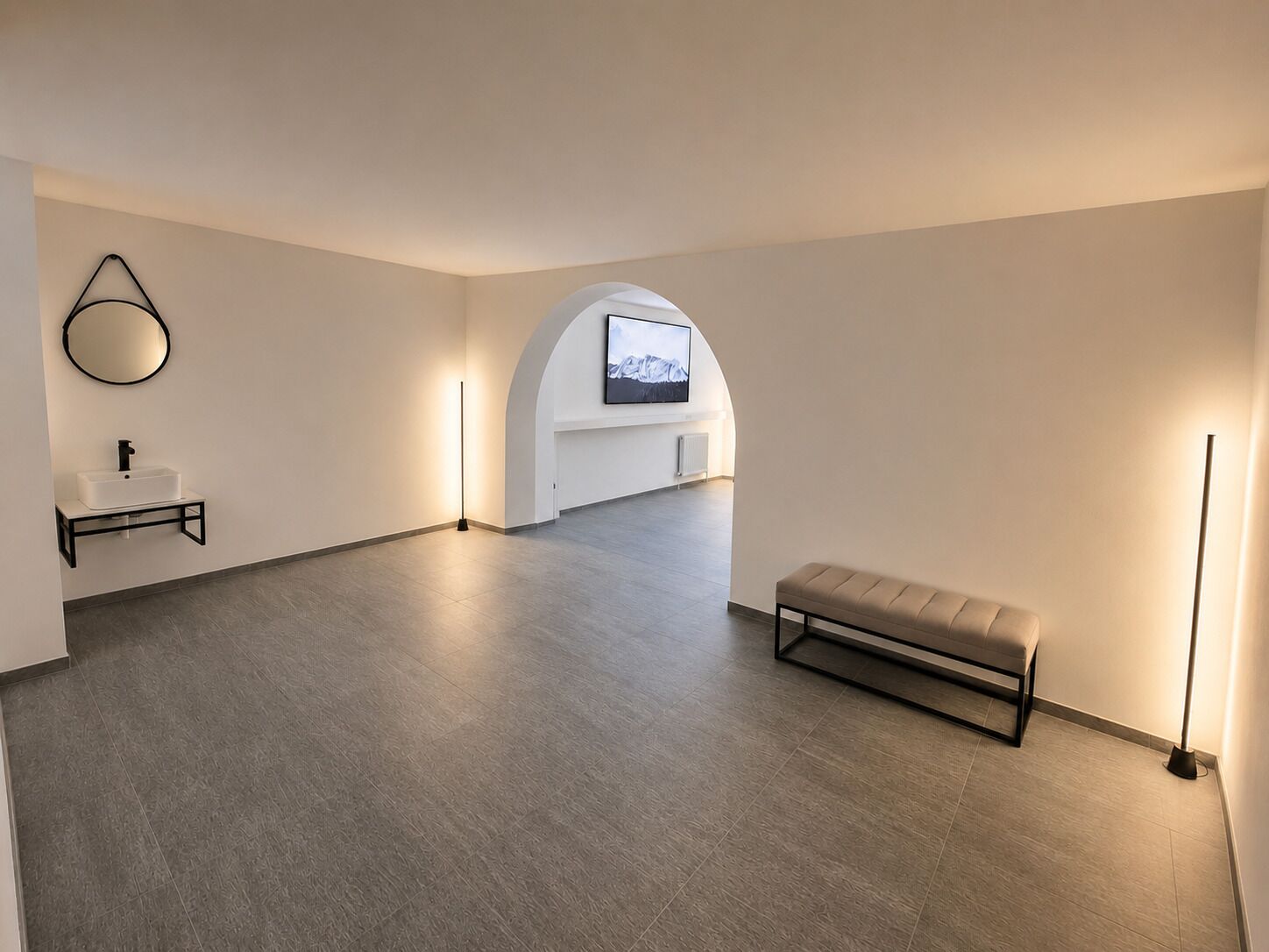 A spacious room with a minimalist design, featuring a bench, a wall-mounted TV, and a floor lamp.